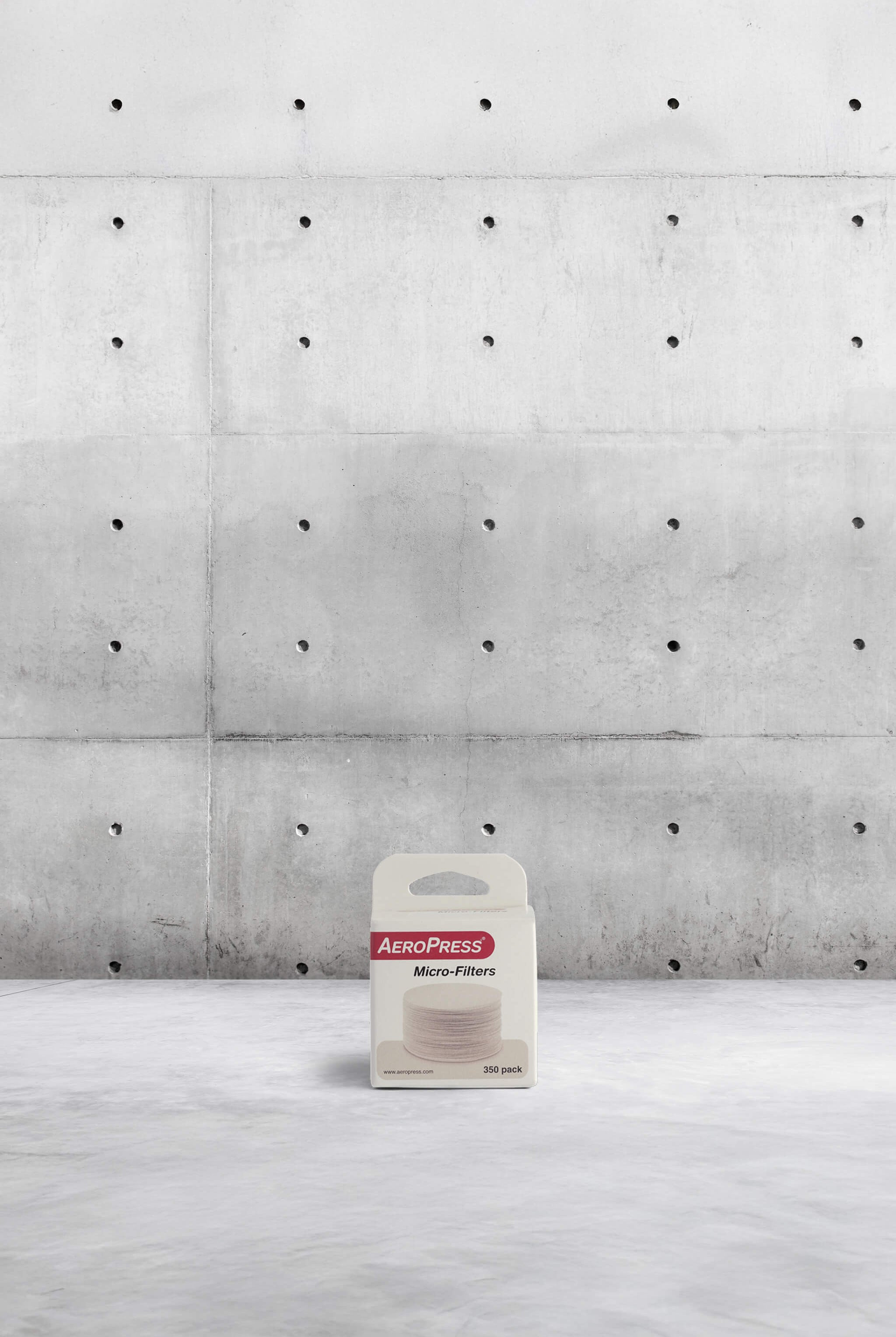 AeroPress micro-filters packaging on a concrete floor with a concrete wall background