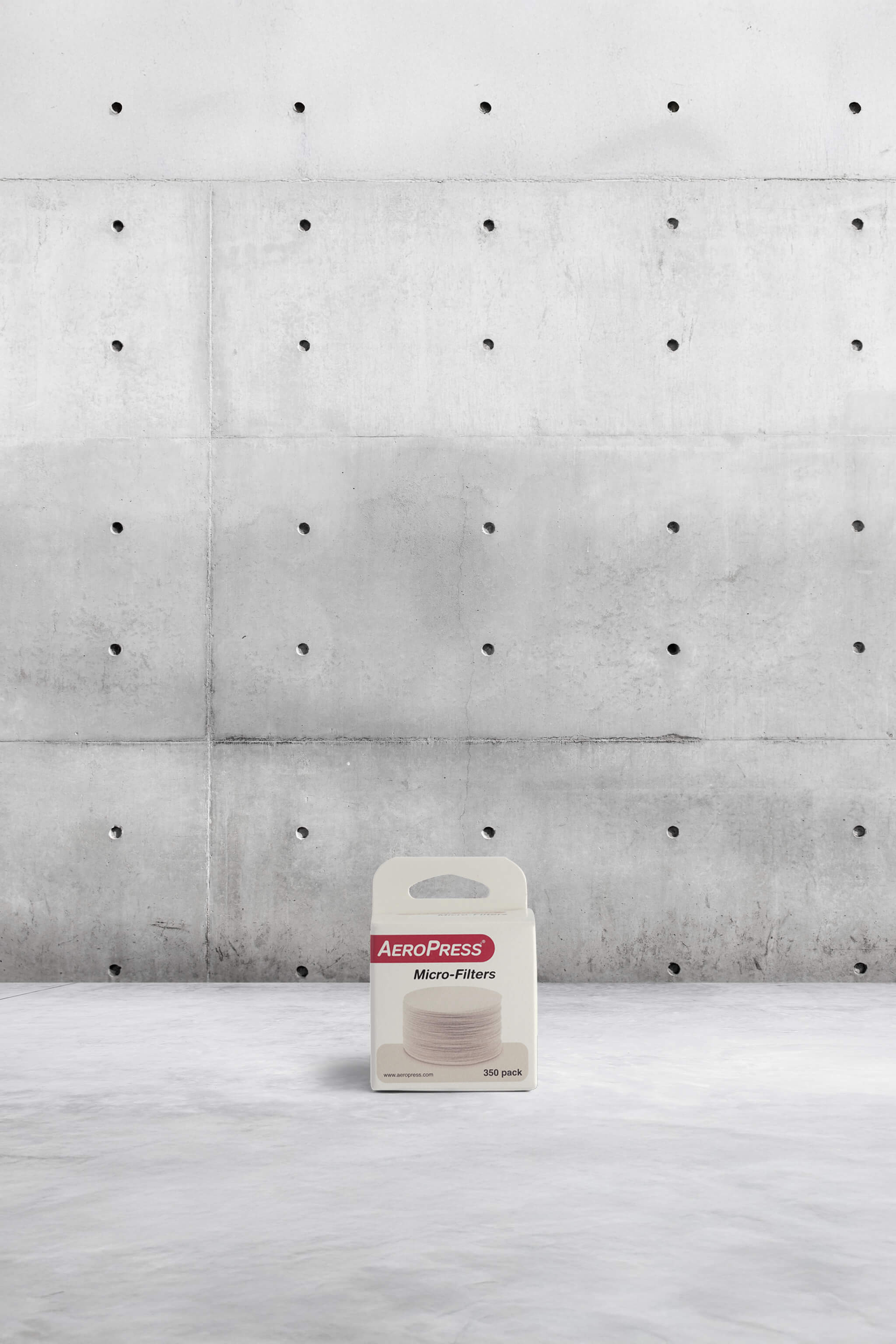 AeroPress micro-filters packaging on a concrete floor with a concrete wall background