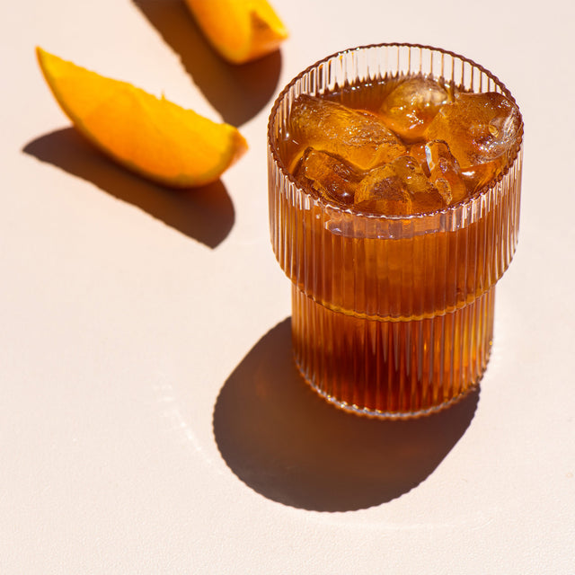 Tumbler of Cold Brew Coffee with ice with orange slices in the background
